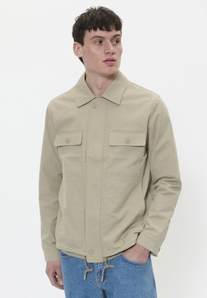 Veste beige légère avec un col, deux poches avant et un ourlet à cordon de serrage. Texture lisse, design minimaliste.