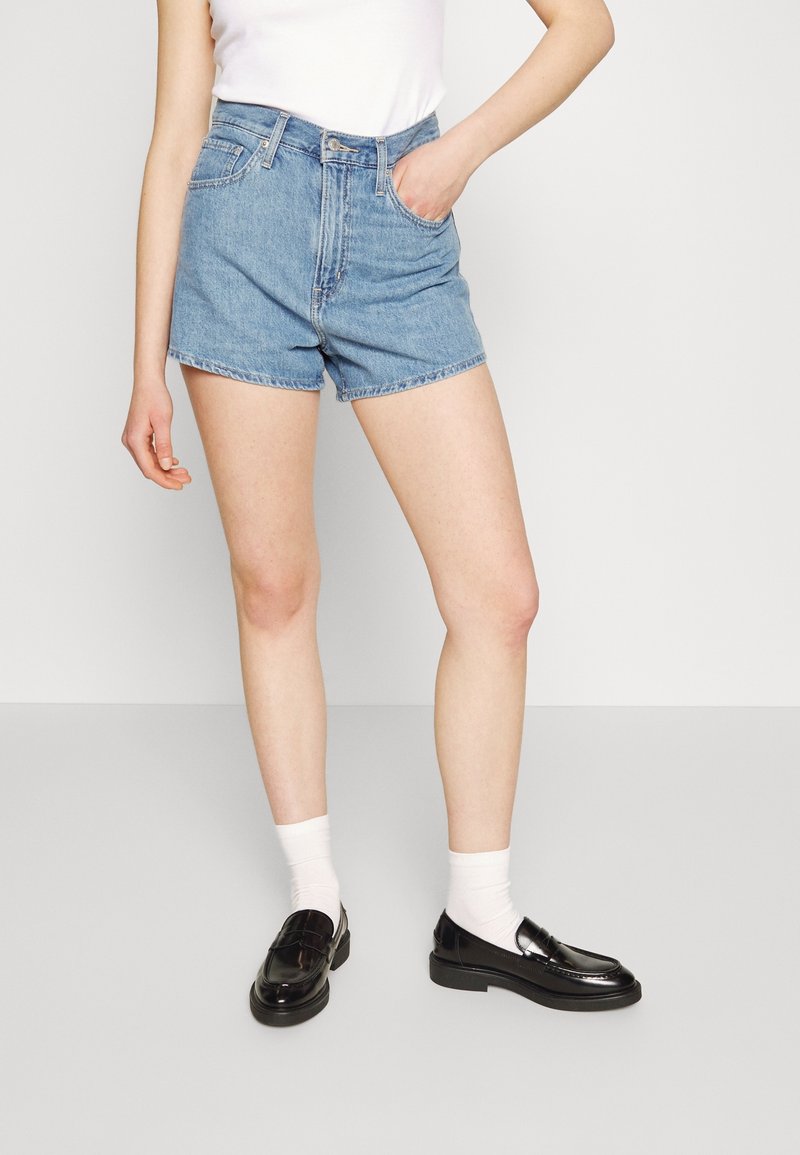 Shorts en jean taille haute de couleur bleu clair, avec des poches avant et un ourlet net. Associés à des mocassins noirs et des chaussettes blanches à la cheville.