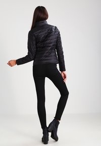 Sort puffjakke med en tætsiddende pasform, der har et vertikalt quiltet mønster og høj krave, parret med sorte skinny jeans og ankelstøvler.