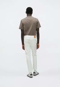 Καφέ βαμβακερό t-shirt, λευκό στενό παντελόνι με πίσω τσέπες και μαύρα σανδάλια. Μινιμαλιστικός σχεδιασμός με δερμάτινο αυτοκόλλητο στο παντελόνι.