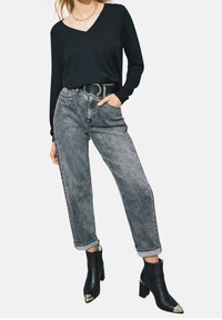 Maglione nero a scollo a V, jeans grigio chiaro a vita alta con risvolti e stivaletti neri con punte metalliche.