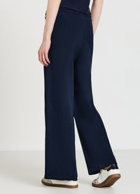 Marineblaue weite Hosen mit einem elastischen Bund, weichem Stoff und entspannter Passform, kombiniert mit weißen und beigen Sneakern.