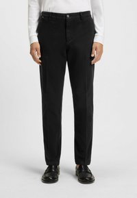 Czarne spodnie materiałowe o gładkim wykończeniu, z klasycznym krojem, przednimi kieszeniami i zapięciem na guzik. W zestawie z czarnymi mokasynami.