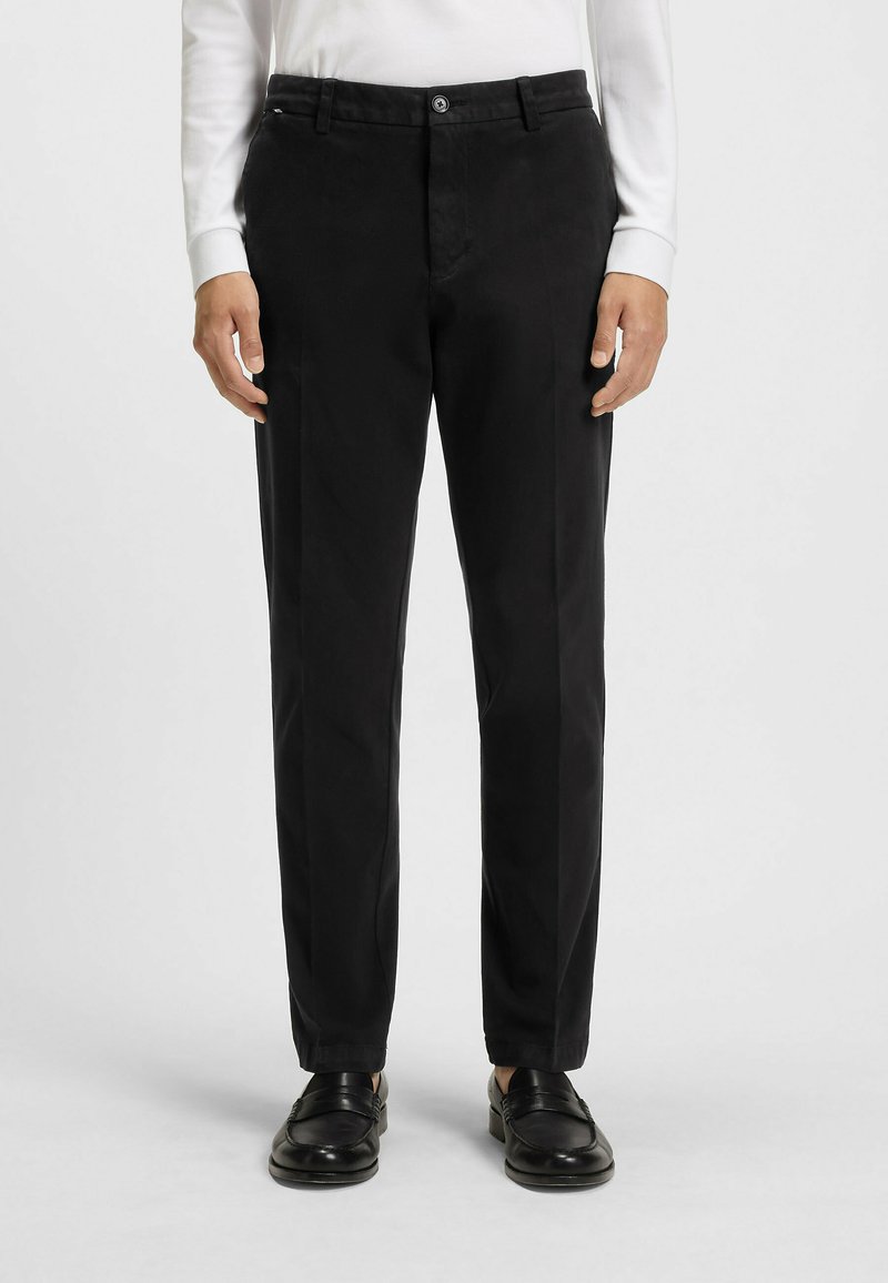 Czarne spodnie materiałowe o gładkim wykończeniu, z klasycznym krojem, przednimi kieszeniami i zapięciem na guzik. W zestawie z czarnymi mokasynami.