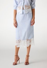 Fustă din in bleu deschis, cu un tiv din dantelă albă, având o siluetă ajustată și modele florale delicate. Potrivită cu sandale cu toc maro.