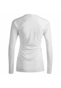 Camicia bianca a maniche lunghe con una texture liscia, cuciture curve e arricciature sui lati, dotata di scollatura rotonda e maniche aderenti.