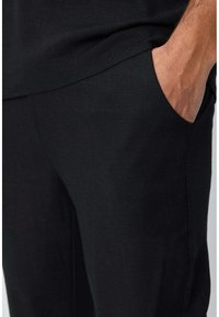 Pantalons en lin noirs avec une poche latérale, texture lisse et coupe droite. Le tissu présente une surface subtile et sans embellissement.