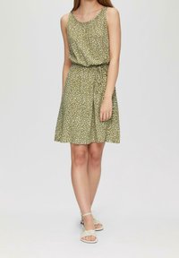 Ärmläns klänning i olivgrön med vita prickar, rynkad halsringning, elastisk midja och utsvängd nederkant. Matchad med strapsandaler i ljus nyans.