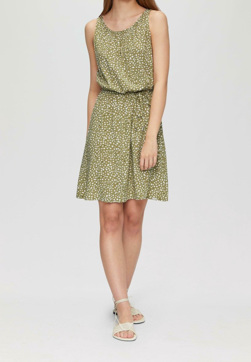 Ärmläns klänning i olivgrön med vita prickar, rynkad halsringning, elastisk midja och utsvängd nederkant. Matchad med strapsandaler i ljus nyans.
