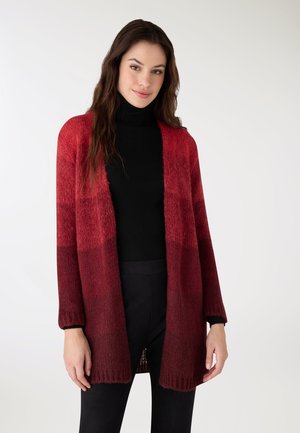 Cardigan lungo in sfumature degradate di rosso e bordeaux, realizzato in morbido materiale a maglia con apertura frontale e maniche lunghe. Dolcevita nero sotto.
