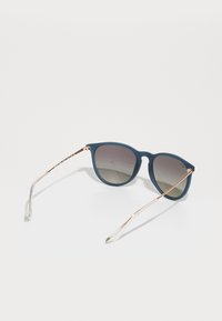 Ochelari de soare supradimensionați cu ramă mată de un albastru închis, lentile gri cu gradient și brațe metalice subțiri de aur roz cu vârfuri transparente.