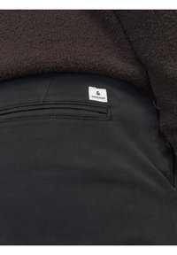Svarta byxor med en slät yta, med en bakficka och en liten vit etikett som säger "JACK & JONES" nära midjan.