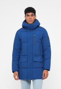 Modrá prošívaná parka s vysokým límcem, na zip uzavíratelnou hrudní kapsou a dvěma předními kapsami. Disponuje kontrastním černým kováním a texturovanou tkaninou.
