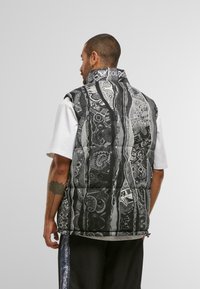 Gilet sans manches matelassé en noir et blanc avec des motifs géométriques. Col haut, côtés zippés et texture de tissu douce.