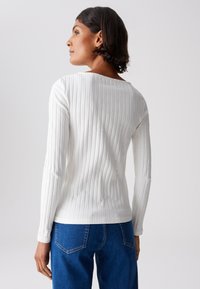 Weißes, geripptes Langarmtop mit weitem Ausschnitt, kombiniert mit jeansblauen Jeans im klassischen fünf Taschen-Design und sichtbaren Nähten.