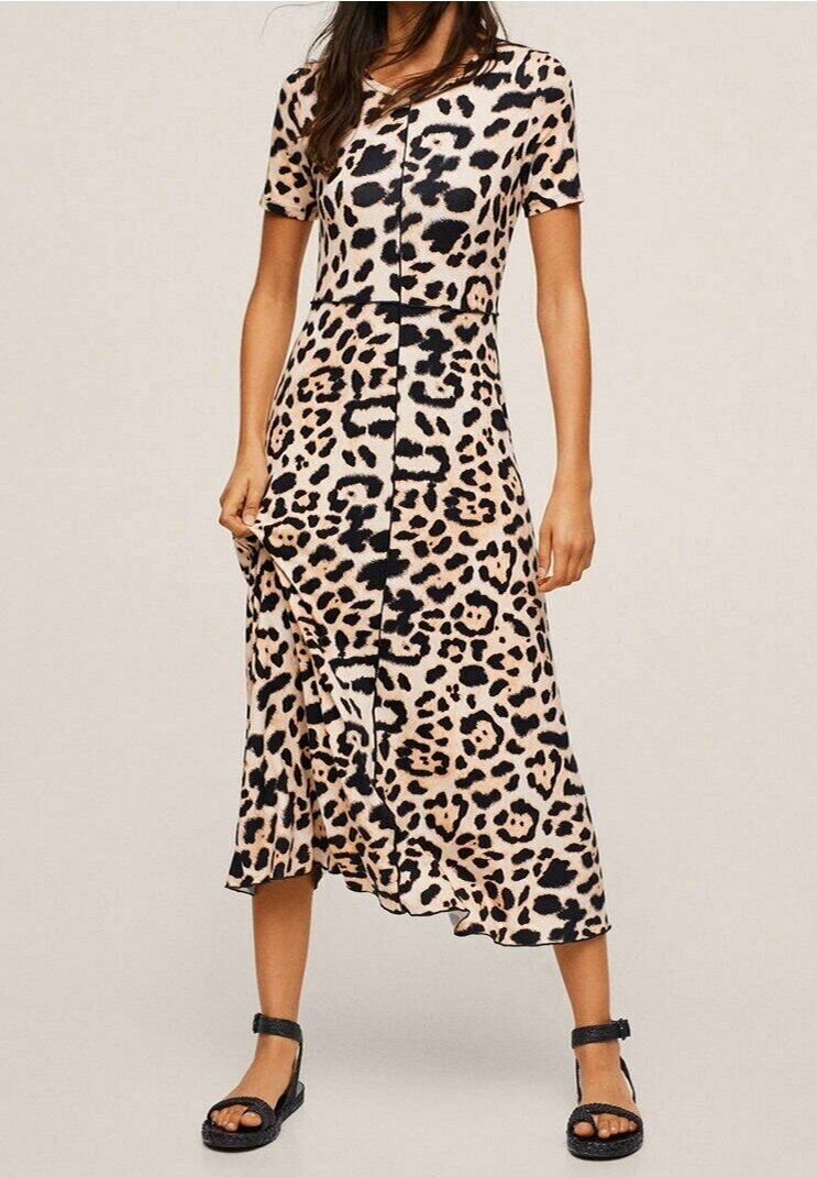 Femme portant une robe léopard à manches courtes et longueur midi, assortie à des sandales à brides noires, sur un fond uni.