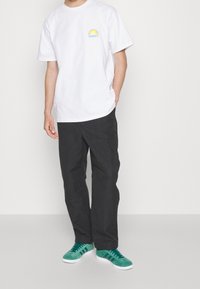 Wit katoenen T-shirt met een kleine zonafbeelding, gecombineerd met zwarte cargobroek en groene sneakers. Eenvoudig ontwerp met een losse pasvorm.