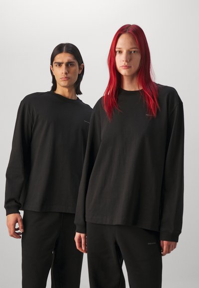 To personer har på seg svarte langermede skjorter og matchende svarte bukser. Stoffet ser mykt ut med en avslappet passform. Minimal merkevare er synlig.