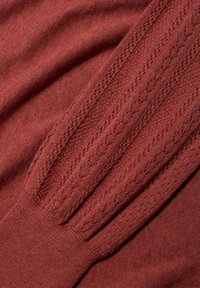 Maglione lavorato a maglia color marsala con maniche a costine texturizzate, dettagli raffinati lungo i bordi e una finitura morbida e liscia.