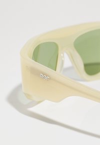 Translucent yellow sunglasses with green lenses, textured frame, and silver "RSF" logo on the side, featuring angular design and smooth finish.