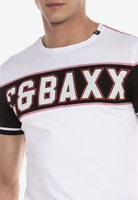 Witte T-shirt met korte mouwen, voorzien van een zwart-rode grafische band met "C&BAXX" in grote, vette letters. Gemaakt van katoen, met een ronde hals.