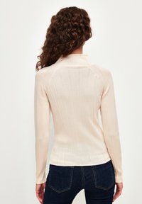Hellbeige, gerippter Langarmoberteil mit hohem Kragen und taillierter Silhouette, das über eine subtile Textur und eine glatte Oberfläche verfügt.