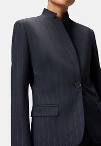 Blazer navy a righe con colletto a incastro, chiusura frontale con bottoni e tasche. Vestibilità sagomata e tessuto dalla texture liscia.