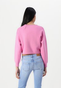 Pull cropped rose avec de longues manches bouffantes, texture tricotée et col rond, associé à un jean ajusté bleu clair.
