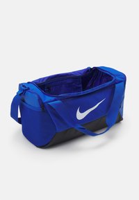 Sinine matkakott, millel on tugeva disain, suure valge Nike logo, ülemine tõmblukk ja kahekordsed kandmisrihmad, mustal põhjal.