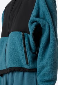 Giacca in fleece verde acqua con parte superiore in nylon nero, chiusura con zip e tasche laterali. Presenta un tessuto testurizzato e un design corto.