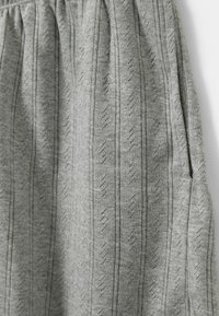 Sivi pleteni materijal s vertikalnim prugama i dijamantnim uzorkom. Ima elastičnu traku u struku i bočne džepove. Mekana tekstura.