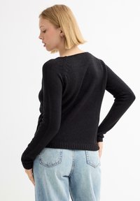 Suéter negro de punto con mangas largas y un diseño ajustado. Presenta un dobladillo acanalado y un sutil detalle en la parte de atrás, combinado con jeans azul claro.