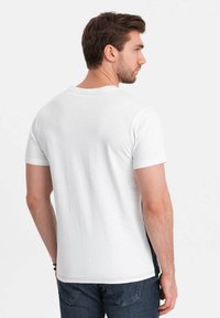 Camiseta de manga corta blanca con cuello redondo, que presenta un panel lateral en negro contrastante y una textura de algodón suave.