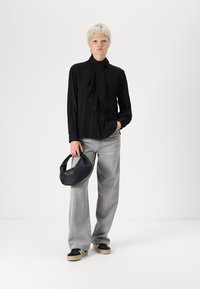 Svart ribbade skjorta med knapplist och slipsdetalj, ljusgrå vida jeans, svart väska, svarta sneakers med beige sulor, och kort platinablont hår.