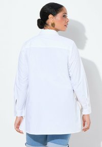 Witte langemouwen shirt van lichtgewicht katoen, met een knoopmanschette en zijsplitten. De achterkant toont een eenvoudig, schoon ontwerp.