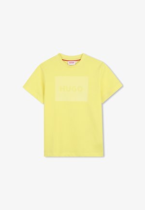 T-shirt jaune à manches courtes et col rond, avec un logo "HUGO" discret imprimé à l'intérieur d'un rectangle jaune légèrement plus clair sur la poitrine.