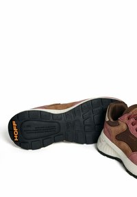 Een paar bruine en roze suède sneakers met een zwarte rubberen zool, het "HOFF"-logo in oranje op de zool en een witte schokdempende tussenzool.