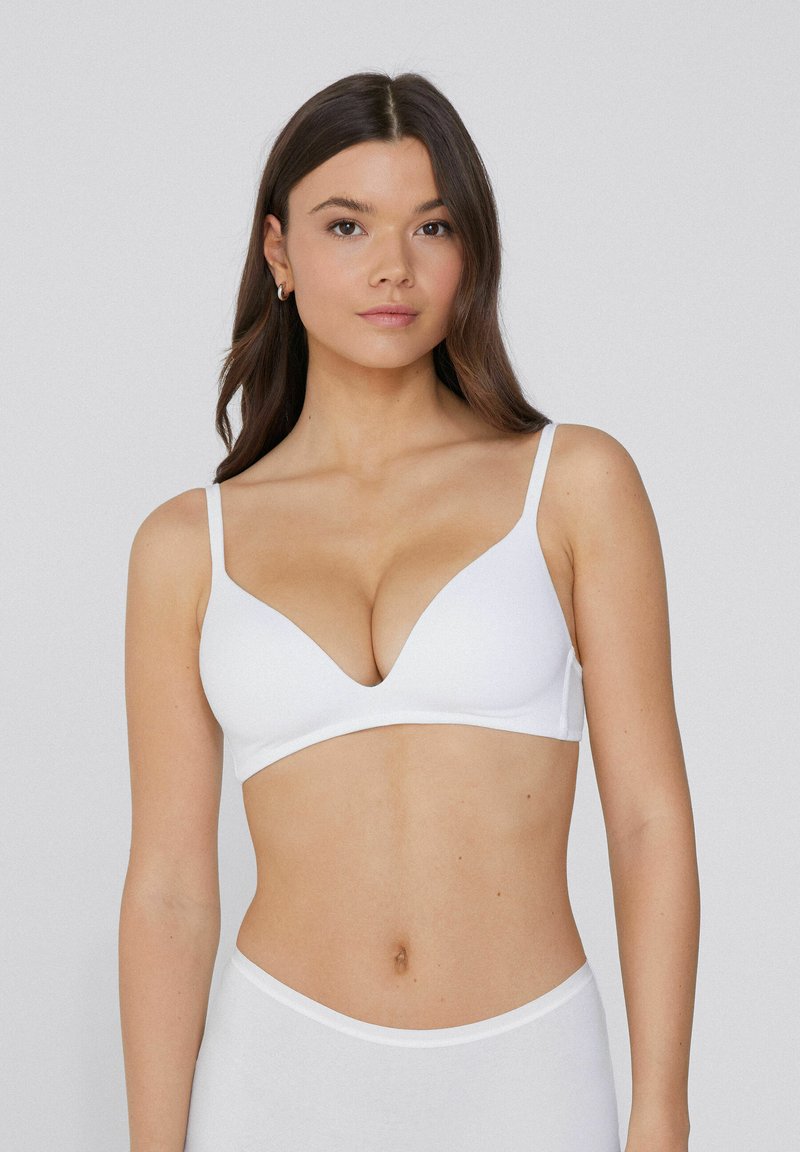 Sujeción inalámbrica blanca con tirantes finos, escote en V y diseño sin costuras. Tela suave y lisa con un acabado mate.