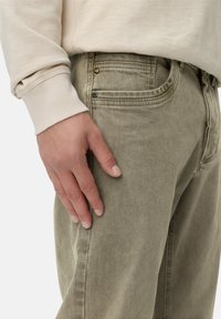 Beige sweatshirt med ribbede manchetter, parret med lys olivegrønne, teksturerede, lige ben bukser. Har forlommer og en metalknap.