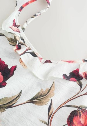 Mönstrad blommig ärmlös topp i lätt, rynkad vit tyg med nyanser av rött och grönt. Har en volangutskärning vid halsen och justerbara axelband.