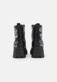 Bottes basses en cuir noir avec une semelle épaisse, ornées de motifs graphiques de style graffiti en gris sur les côtés et une fermeture éclair à l'arrière.