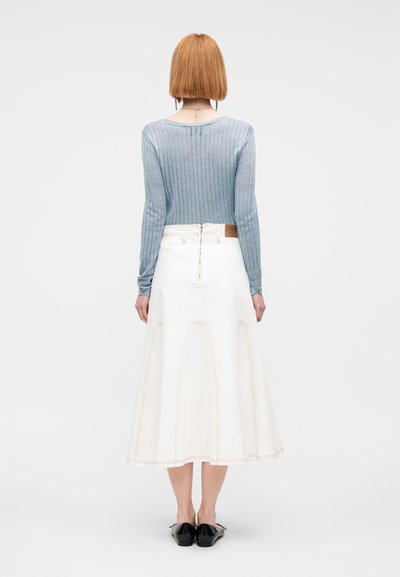Haut en maille côtelée bleu clair à manches longues, associé à une jupe évasée crème avec des coutures courbes, porté avec des chaussures noires sans lacets.