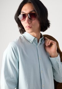 Light blue and white striped button-up shirt with a collar, paired with brown tortoise shell sunglasses. The fabric appears smooth.