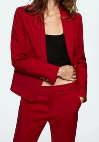 Blazer rosso su misura con chiusura a un bottone, rever a punta e spalle strutturate, abbinato a un top a maniche corte nero a coste.