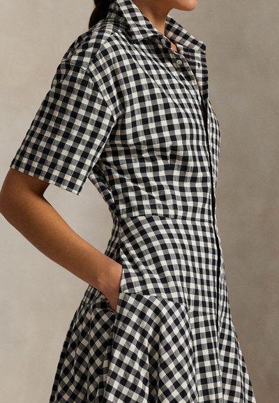 Juoda ir balta languota suknelė su trumpomis rankovėmis, prigludusiu liemeniu ir platėjančia sijono dalimi. Suknelė turi apykaklę ir šonines kišenes.