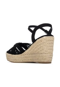 Sandalia de cuña de ante negro con plataforma de yute trenzado y correa al tobillo con cierre de hebilla, vista lateral sobre fondo blanco.