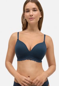 Sostén azul de canalé con bordes de encaje, que presenta una forma de escote en V profundo y tirantes ajustables. Textura de tela suave y acentos de encaje floral.