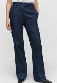 Ciemnoniebieskie spodnie dżinsowe o prostych nogawkach, z przednimi kieszeniami i gładką fakturą. Talia wyposażona w szlufki na pasek.