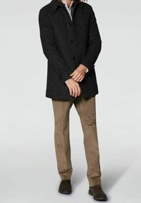 Abrigo negro con patrón de espiga para hombre, con cuello, tres botones y bolsillos laterales, combinado con pantalones de cuadro color camel de pana y zapatos oscuros.