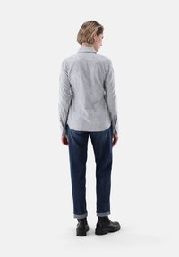 Button-up shirt in light gray with embroidered floral patterns; paired with dark denim pants and black ankle boots. Back view shown.